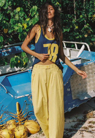 A woman stands outdoors in front of a blue boat and green foliage