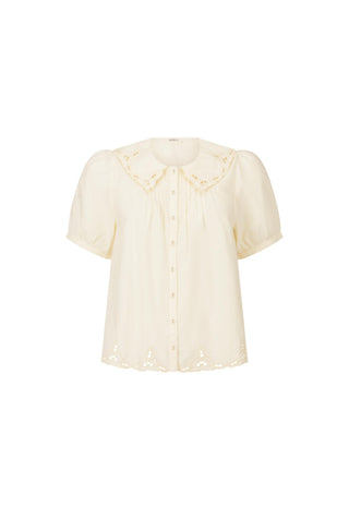 a-cream-colored-short-sleeve-blouse-with-eyelet-lace-detailing-on-the-collar-and-hem-featuring-a-button-down-front-and-gathered-bodice-shown-against-a-plain-white-background