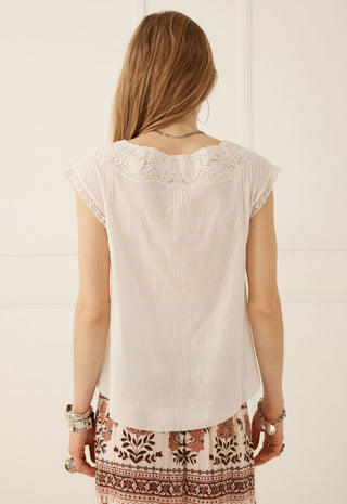 a-woman-viewed-from-behind-wearing-a-cream-colored-short-sleeve-top-with-lace-detailing-around-the-neckline-paired-with-patterned-pants
