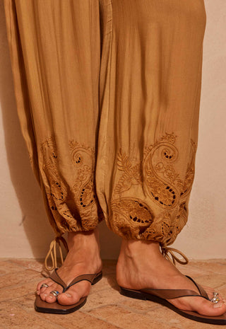 close-up-of-a-person-wearing-loose-tan-harem-style-pants-with-embroidered-paisley-detailing-near-the-ankles-paired-with-brown-thong-sandals-on-a-warm-beige-stone-floor
