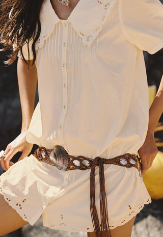 a-close-up-of-a-person-wearing-a-cream-short-sleeve-blouse-with-eyelet-lace-trim-and-matching-cream-shorts-styled-with-a-brown-woven-belt-featuring-cowhide-and-shell-details