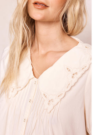 Close-up of a woman wearing a cream-colored blouse with a large eyelet Peter Pan collar and button front.