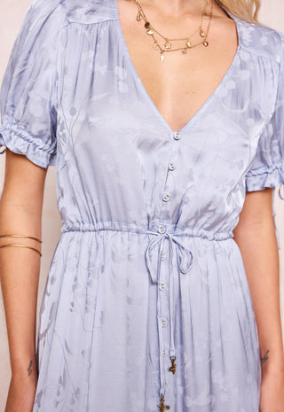 A close-up of a woman wearing a light blue floral print dress with a deep V-neckline, short puff sleeves, and a drawstring waist.