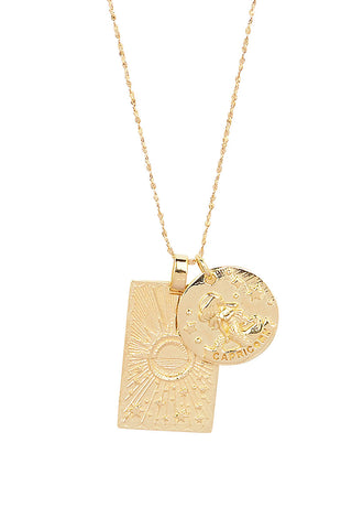 Close up front view of Spell’s Capricorn Stargazer Zodiac Necklace charms. One charm is of a rectangular shape and features a sun with stars while the other charm is circular and features the Zodiac label and icon.