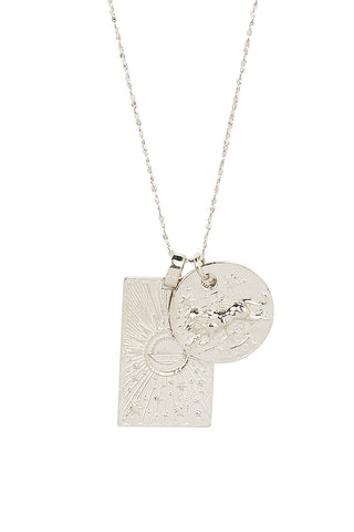 Close up front view of Spell’s Leo Stargazer Zodiac Necklace charms. One charm is of a rectangular shape and features a sun with stars while the other charm is circular and features the Zodiac label and icon.
