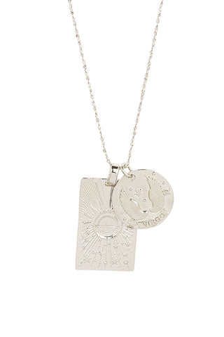 Close up front view of Spell’s Virgo Stargazer Zodiac Necklace charms. One charm is of a rectangular shape and features a sun with stars while the other charm is circular and features the Zodiac label and icon.